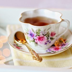 A white tea cup with a floral design sits on a saucer with a gold spoon.
