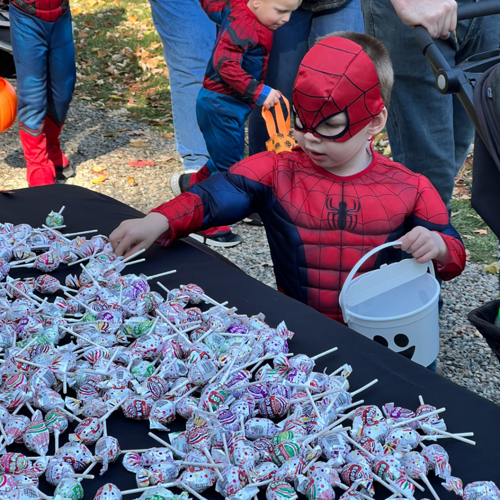 A little boy is dressed as Spider-Man for Halloween and he's picking out lollipops.