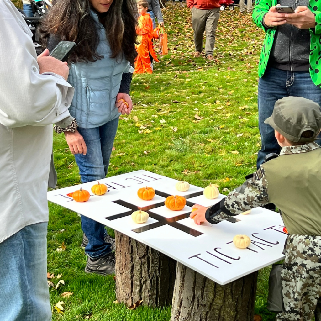 A child plays a giant game of tic-tac-toe using miniature pumpkins as tokens.