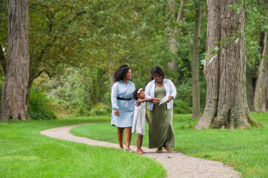 A grandmother, mother, and daughter enjoy a cheerful walk on a wooded path at Ford House.