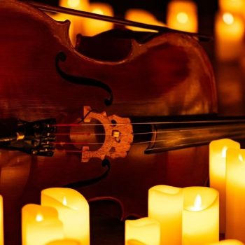 Close up of a cello surrounded by warm candlelight, illustrating the elegant autumn ambiance of the Halloween Concert Over the Cove Kalkaska Quartet at Ford House.