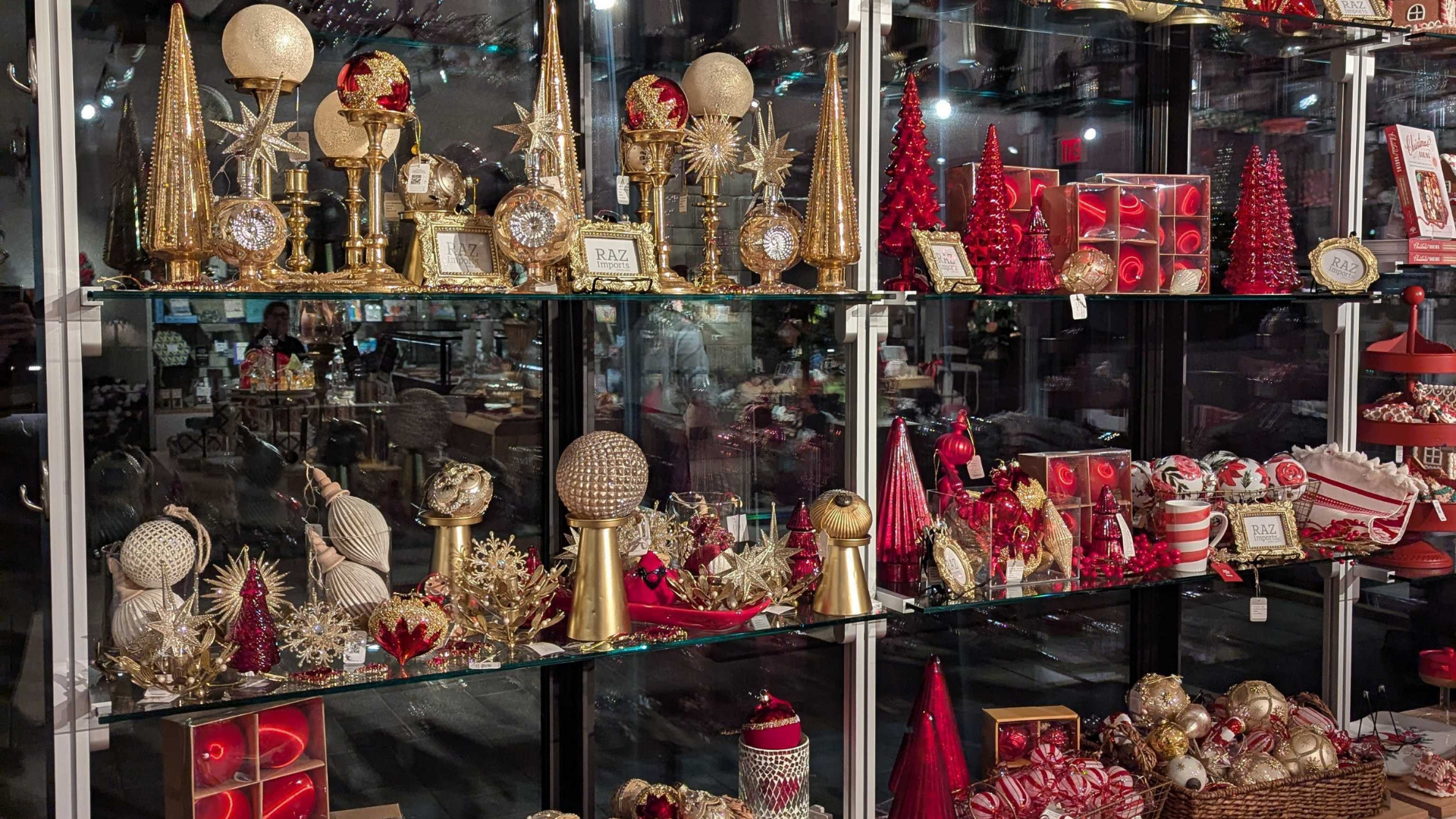 Gold and red glass ornaments, trees and finials arranged on lit glass shelves in The Shop at Ford House.